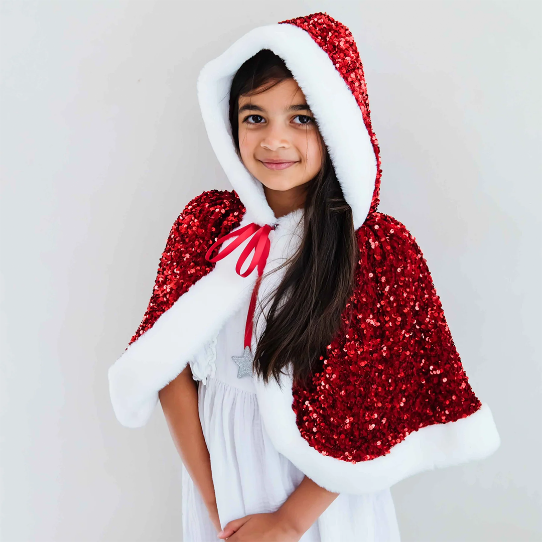 Meisje met lang donker haar draagt de mimi & lula rode Mrs Claus verkleedcape met pailletten en opgezette capuchon.