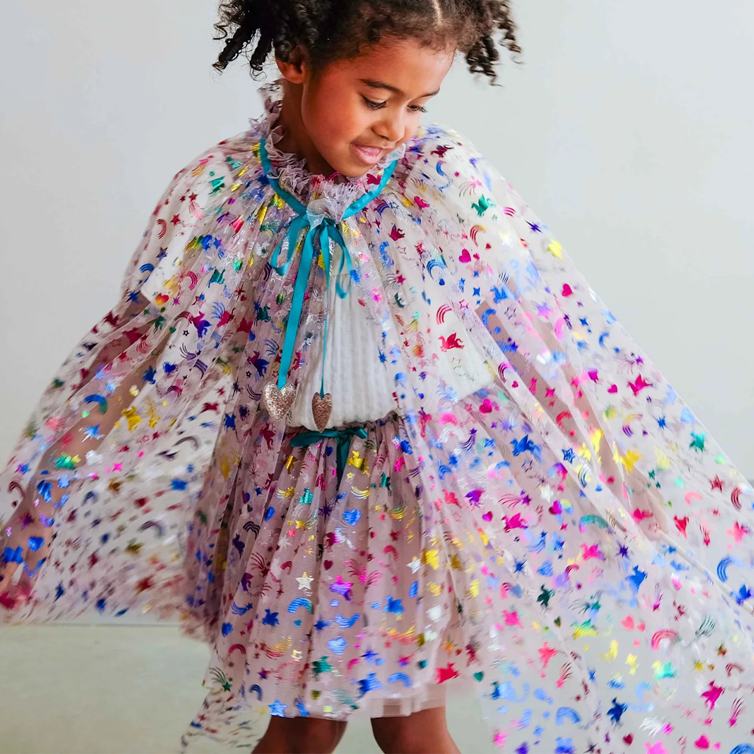 Een kind draagt een veelkleurige verkleedrok en cape met regenboog-, sterren- en eenhoornpatronen.