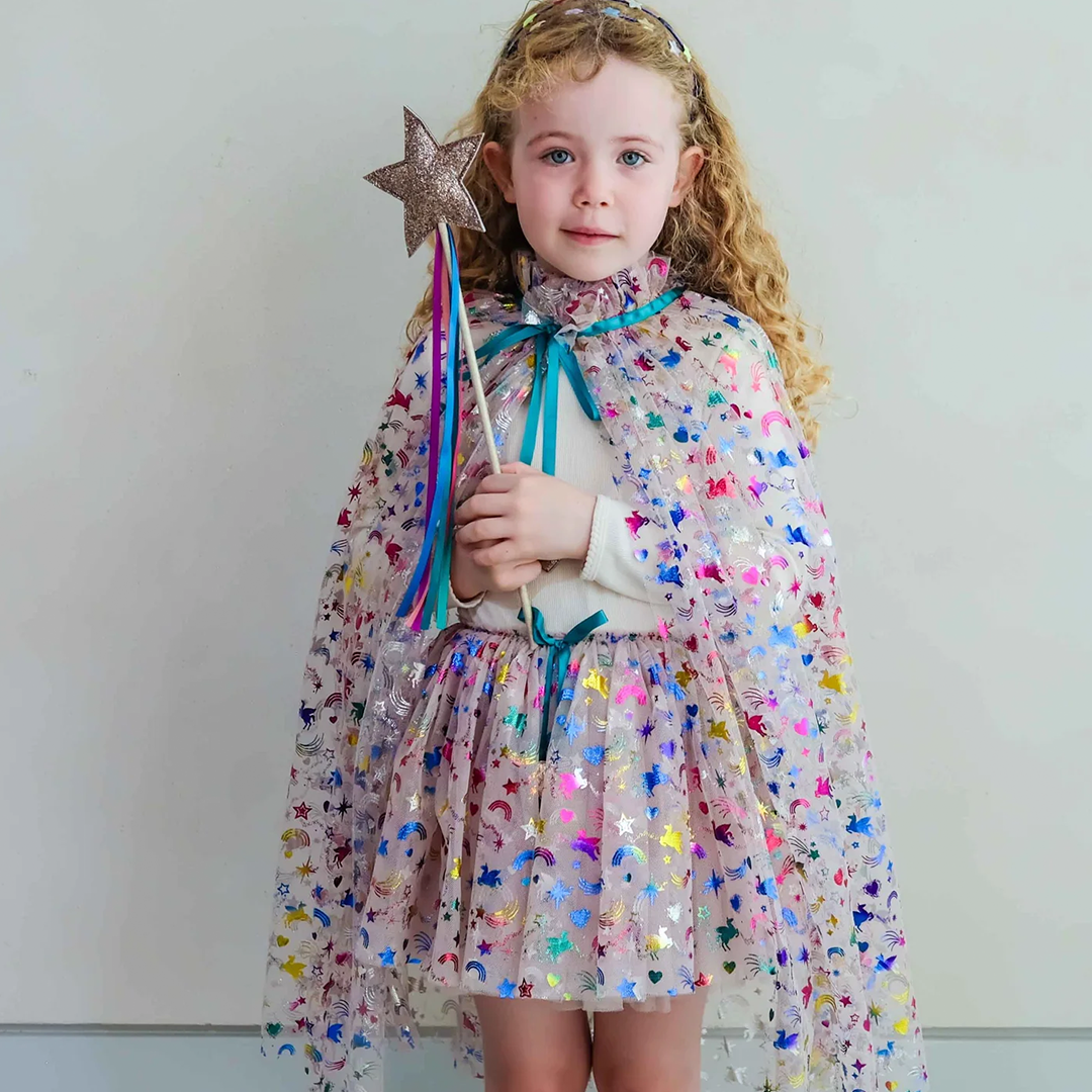Een kind in een veelkleurige verkleedrok en cape met sterren en regenbogen, houdt een glitter toverstaf vast.