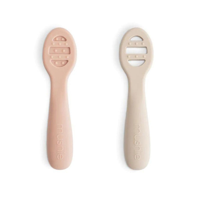 Twee mushie sensorische babylepels in roze en beige met gestructureerde koppen.