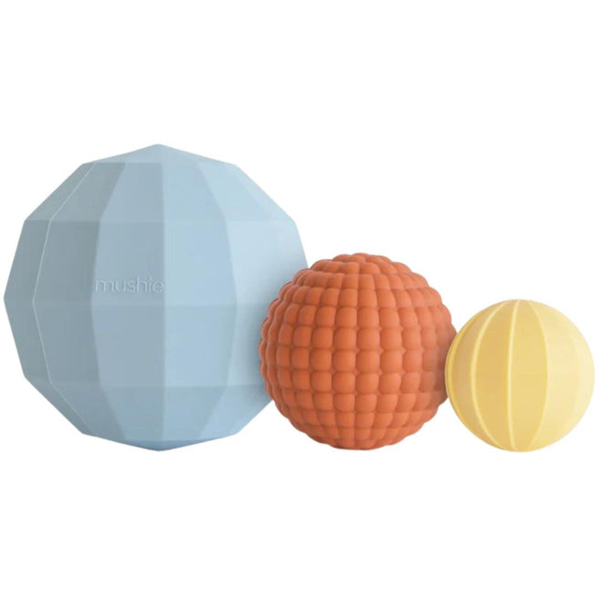 Drie mushie sensorische ballen voor baby's in lichtblauw, oranje en geel met verschillende texturen.