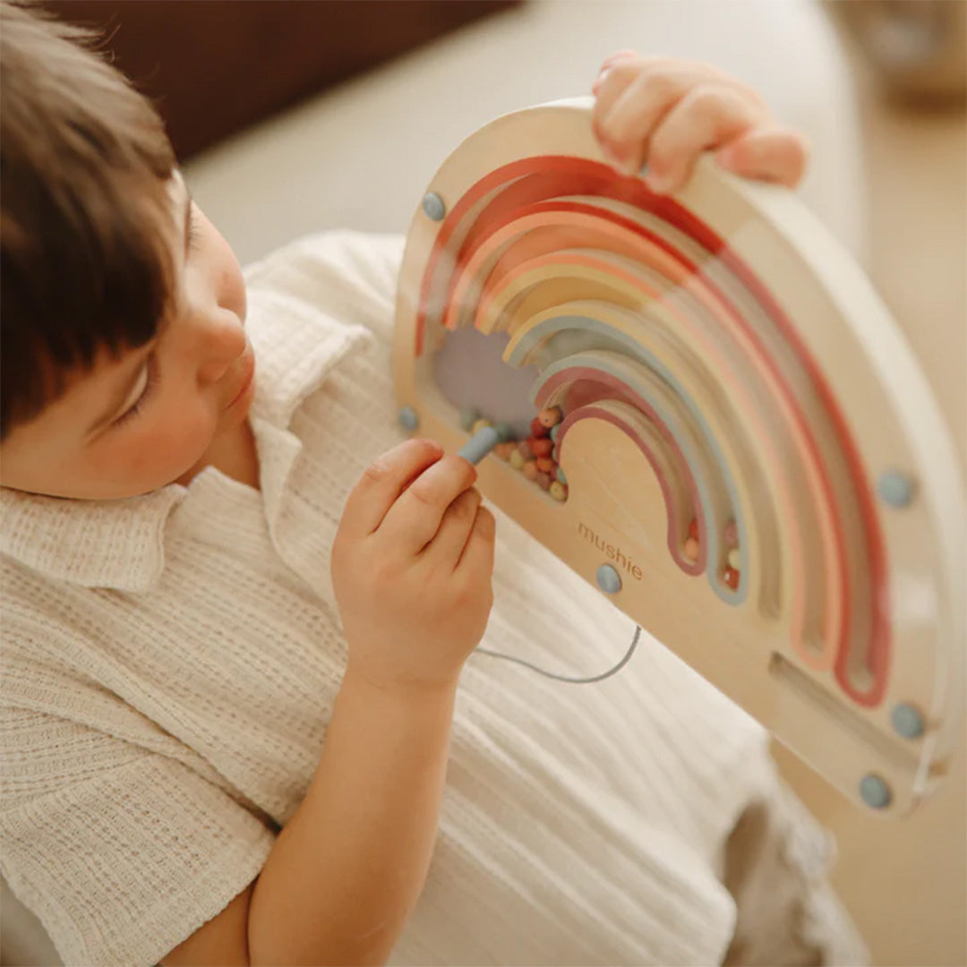 Een kind gebruikt de magnetische pen om de kralen in het mushie houten regenboog doolhof te bewegen.