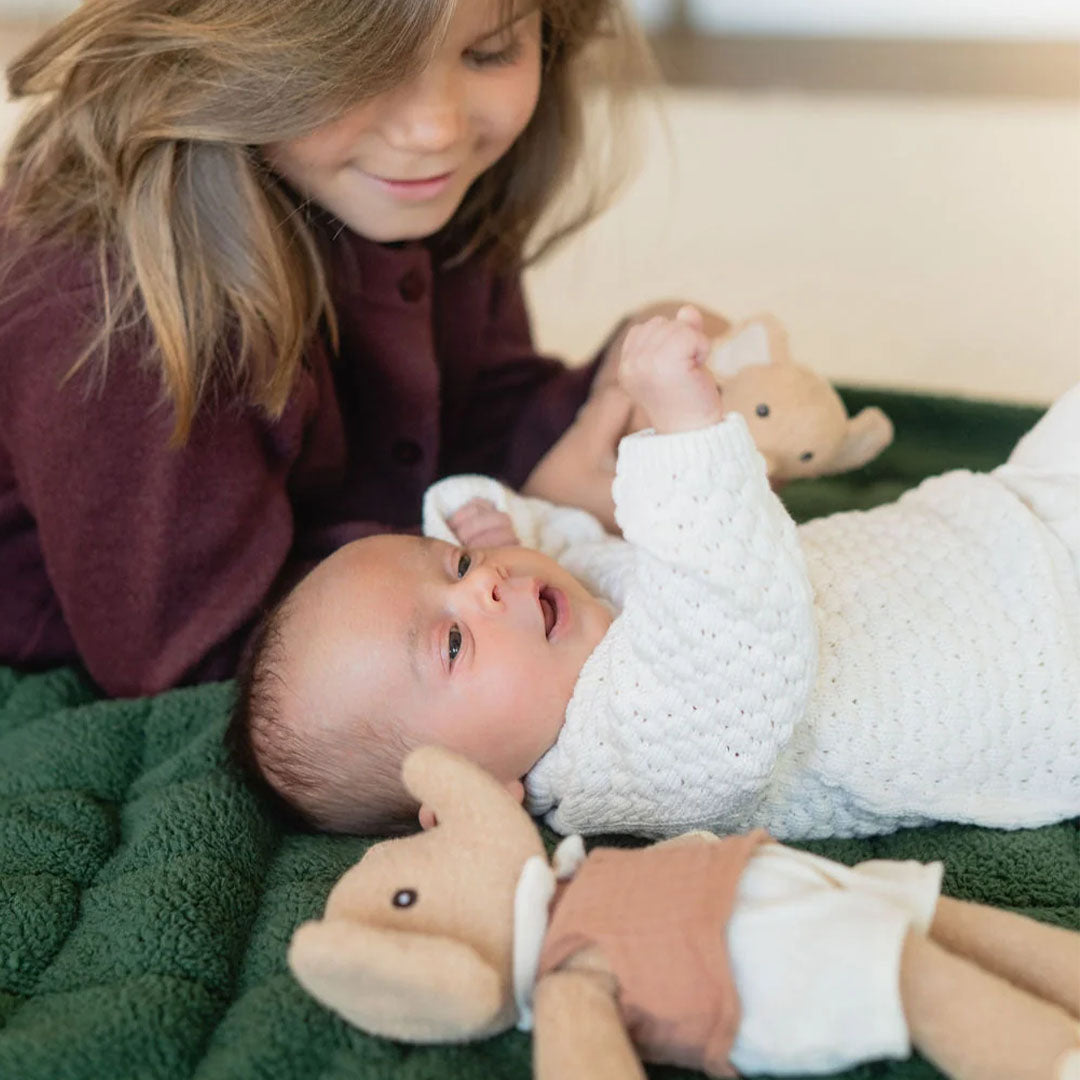 Een baby ligt op het donkergroene teddy babyspeelkleed en kijkt naar een ouder kind.