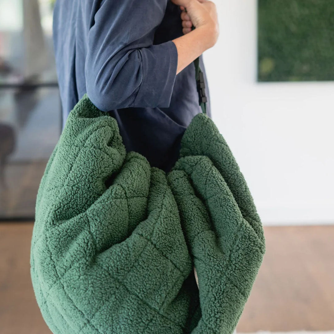 play&go donkergroen teddy babyspeelkleed opgevouwen als tas wordt over de schouder gedragen.