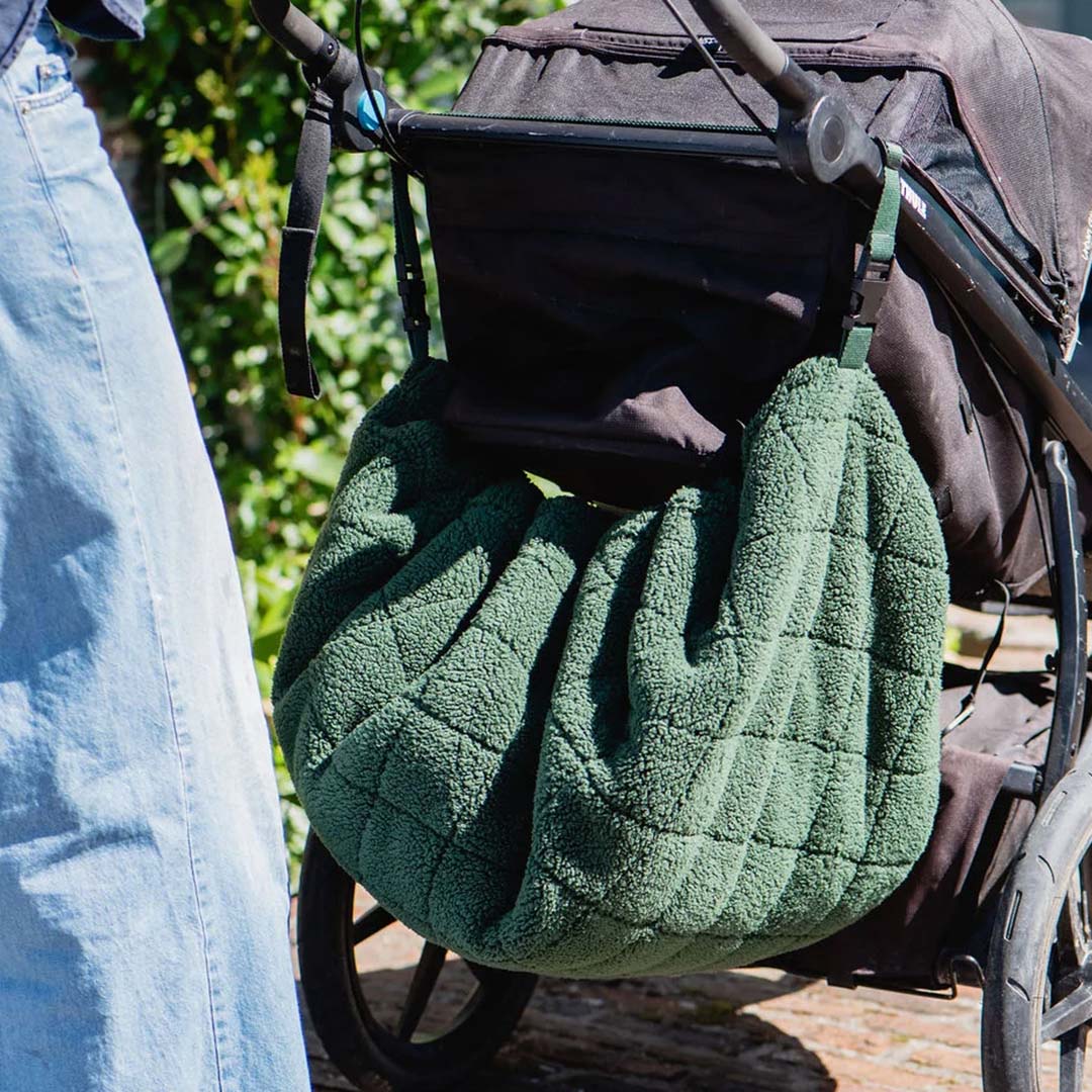 play&go donkergroen teddy babyspeelkleed opgevouwen als tas hangt aan een kinderwagen.