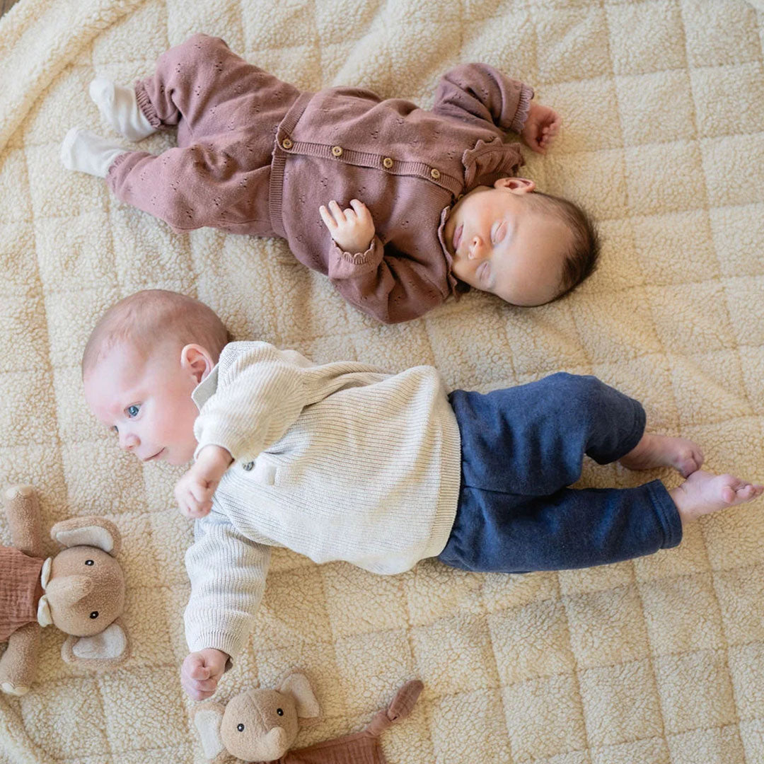 Twee baby's liggen op een beige play&go babyspeelkleed van teddy stof, met twee kleine olifantjes.