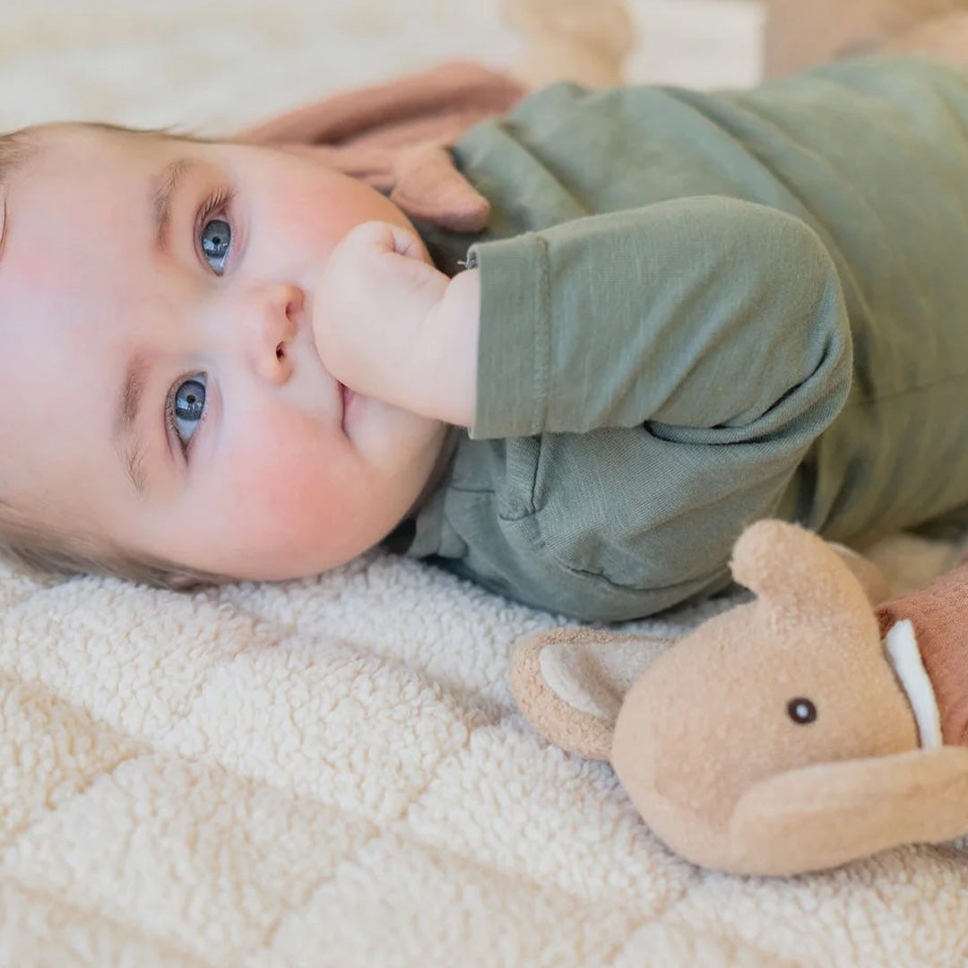 Een baby ligt op een beige play&go babyspeelkleed van teddy stof, met een klein olifantje ernaast.