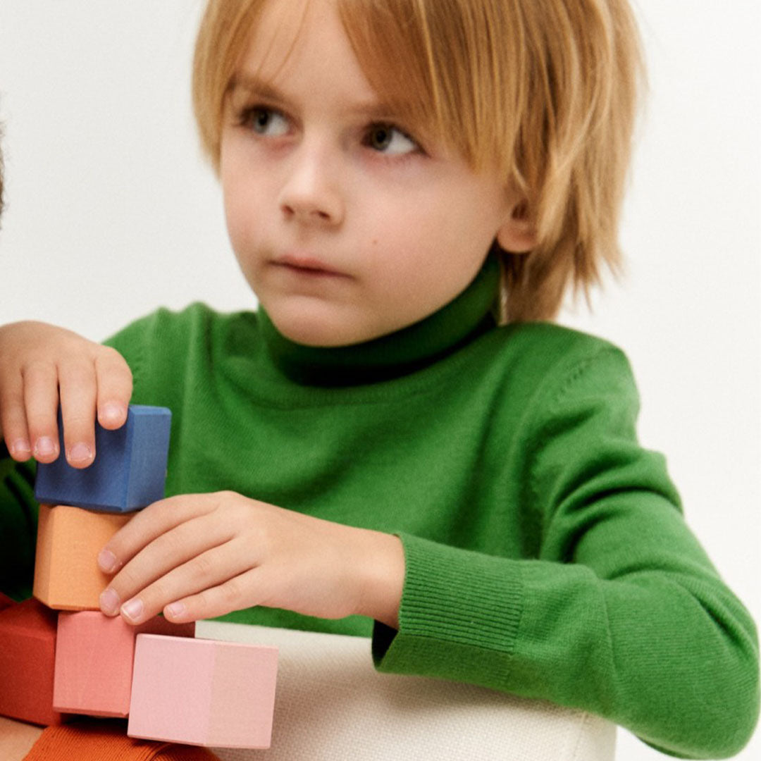 Een kind stapelt Raduga Grëz houten bouwblokken in verschillende kleuren.