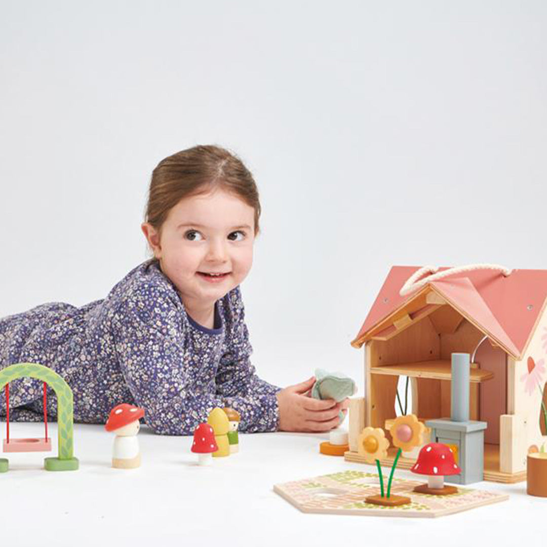 Een lachend meisje speelt op de grond met het houten poppenhuis en de bijbehorende speelset.